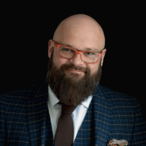 Usmiechnięty Prawnik Bartłomiej Łukomski w oklarach stojący na czarnym tle